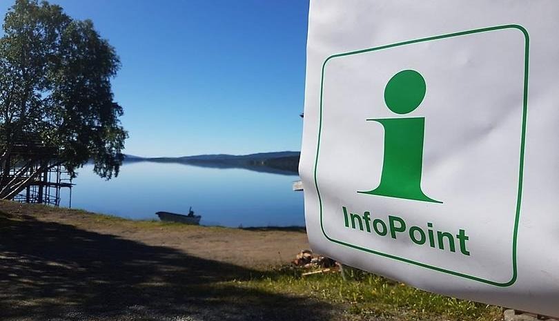 Infopointflagga med sjö och båt i bakgrunden.